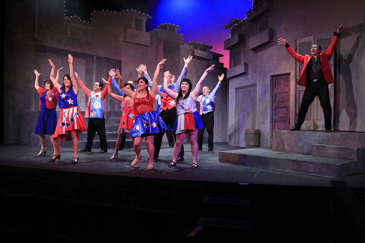 A stage of actors perform a dance routine - arms in the air.