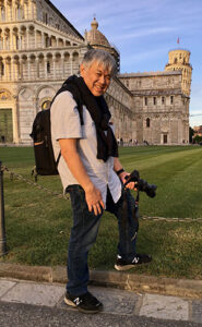 Man standing with a camera in front of the leaning tower of Pisa.