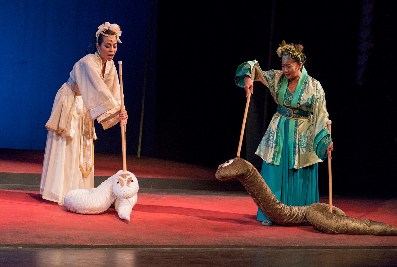 Two female actors manipulate snakes puppets with attached poles.